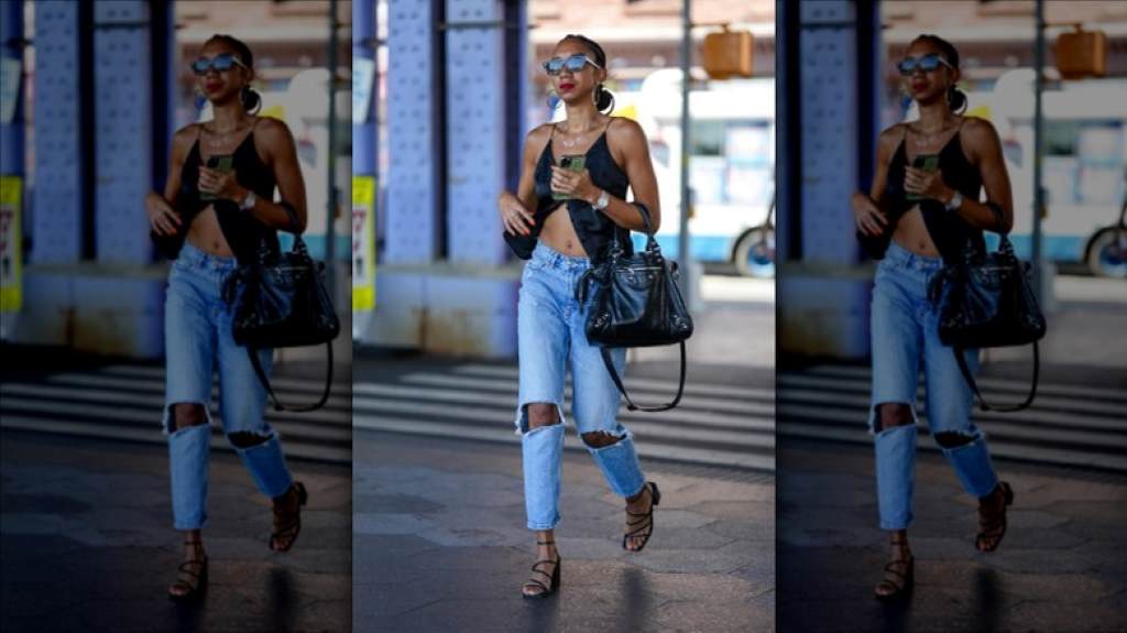 Woman in casual street style wearing a light wash denim vest over a graphic tee and black jeans, accessorized with sneakers.